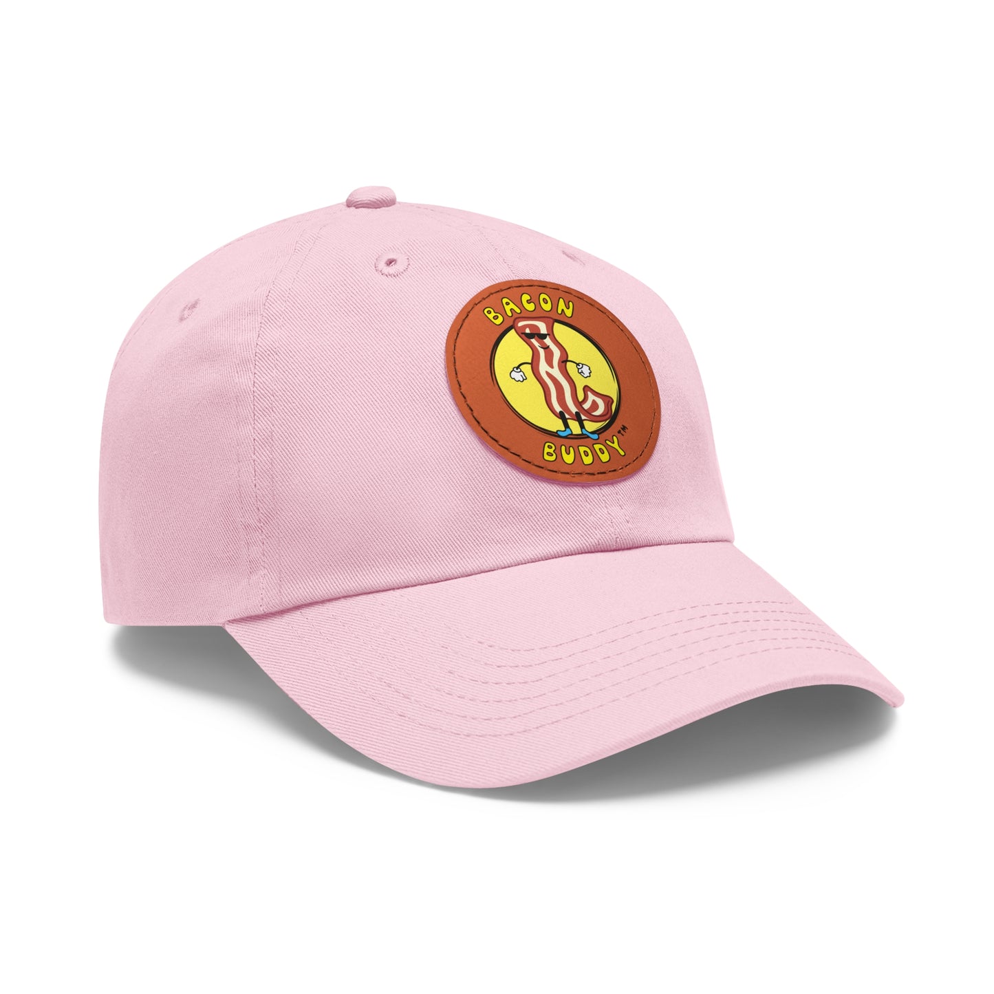 'Dad hat' style Light Pink coloured baseball cap with a round, brown leather patch sewn on the front. Printed on the leather patch is a yellow circular graphic logo of the Bacon Buddy character, a cartoon style strip of bacon with arms, legs and sunglasses. Curved yellow text of Bacon Buddy around the logo. Photographed is front / side view