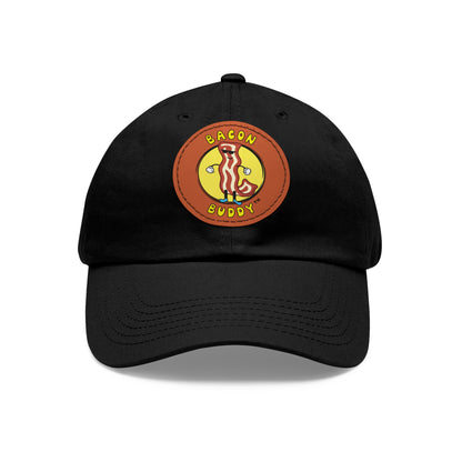 'Dad hat' style Black coloured baseball cap with a round, brown leather patch sewn on the front. Printed on the leather patch is a yellow circular graphic logo of the Bacon Buddy character, a cartoon style strip of bacon with arms, legs and sunglasses. Curved yellow text of Bacon Buddy around the logo. Photographed is front view 