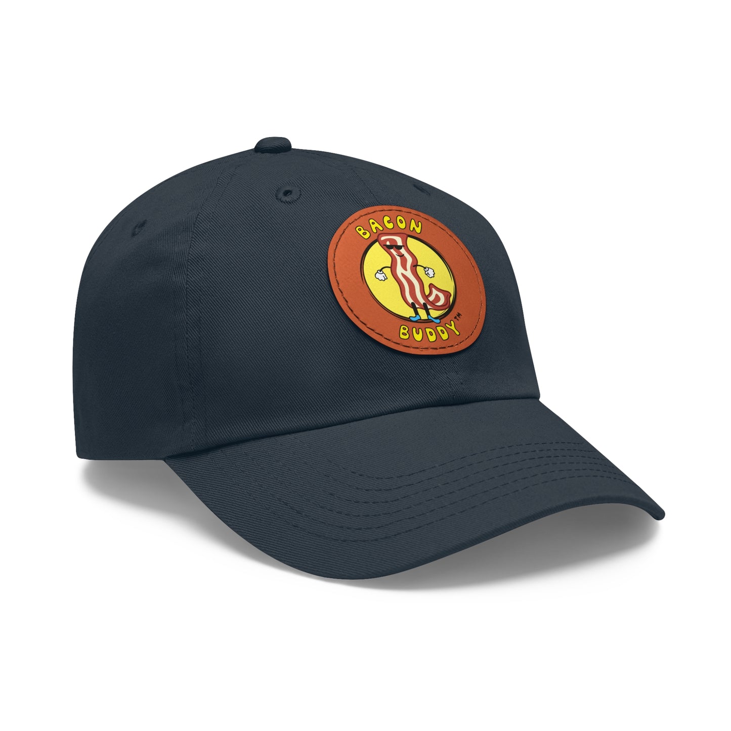 'Dad hat' style Navy coloured baseball cap with a round, brown leather patch sewn on the front. Printed on the leather patch is a yellow circular graphic logo of the Bacon Buddy character, a cartoon style strip of bacon with arms, legs and sunglasses. Curved yellow text of Bacon Buddy around the logo. Photographed is front / side view 