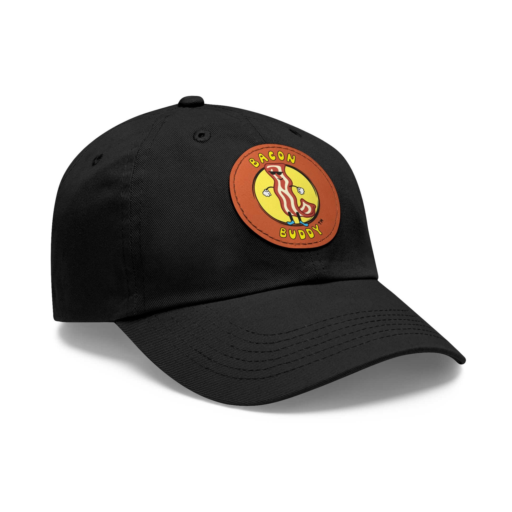 'Dad hat' style Black coloured baseball cap with a round, brown leather patch sewn on the front. Printed on the leather patch is a yellow circular graphic logo of the Bacon Buddy character, a cartoon style strip of bacon with arms, legs and sunglasses. Curved yellow text of Bacon Buddy around the logo. Photographed is front / side view 