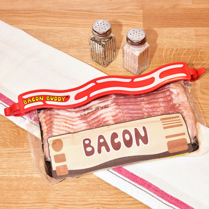 The Bacon Buddy clip, a 13 inch (35cm) long, red wavy bacon shaped plastic food packaging clip. Has printed wavy text in yellow saying 'Bacon Buddy' and wavy cream strips to look like bacon. Clip photographed closing a package of bacon on a kitchen counter top